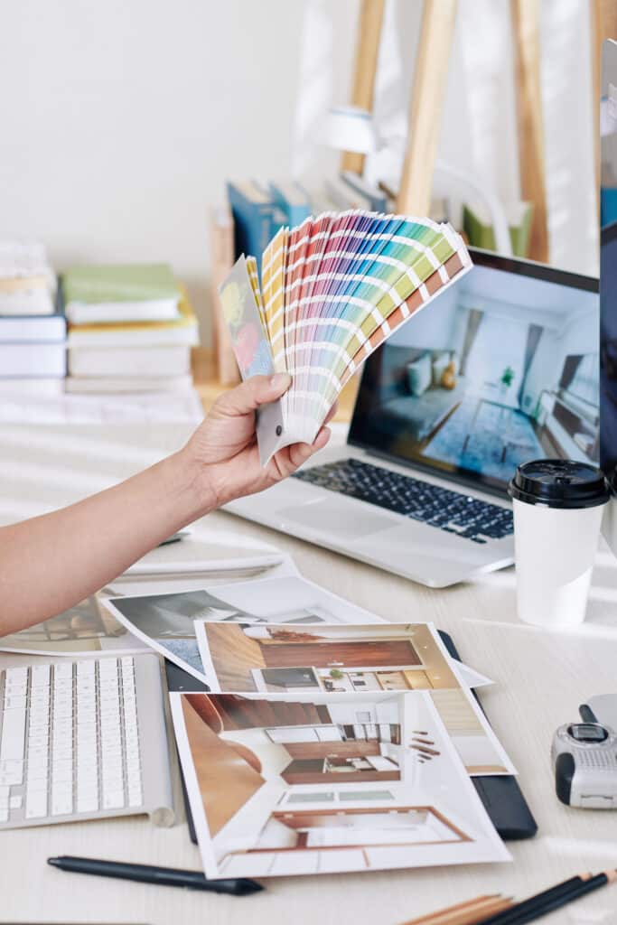 Interior designer working with color palette Femme tenant un nuancier sur un bureau typique d'un cabinet d'architecte avec ordinateur et photographies de projets d'architecture.