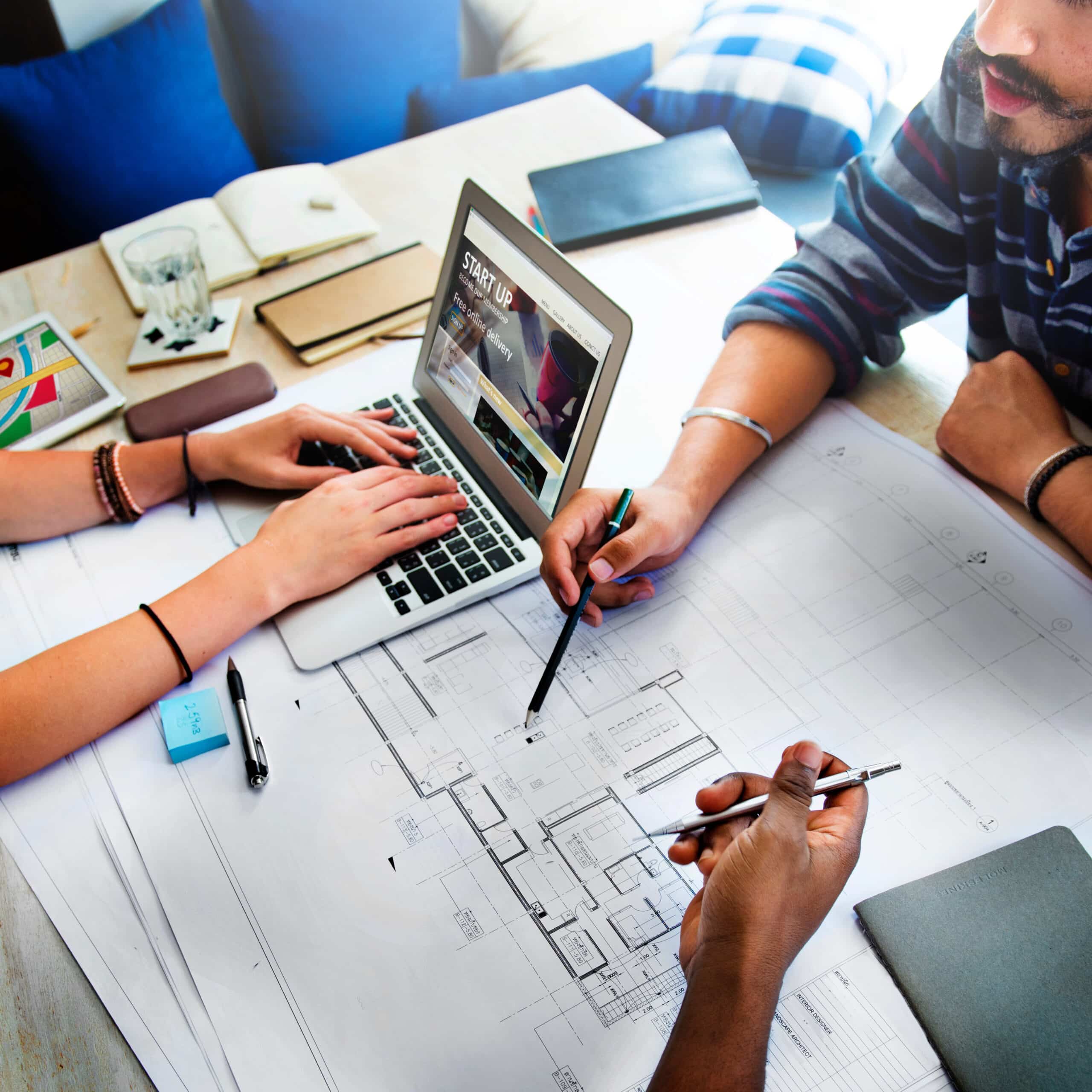 Trois architectes travaillent ensemble sur un ordinateur portable et des papiers dans un cabinet d'architecte.